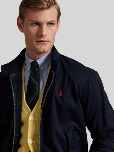 Männermodel trägt Bomberjacke mit Logo-Stickerei von POLO RALPH LAUREN in Dunkelblau mit seitlichen Eingrifftaschen, Nahaufnahme Oberkörper.