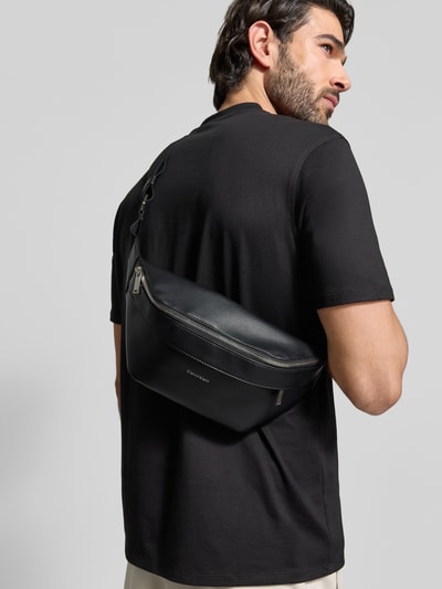 Männermodel trägt Waistbag in Leder-Optik Modell 'Raised' von CK Calvin Klein, schwarze strukturierte Oberfläche, Ganzkörperansicht Rückansicht.