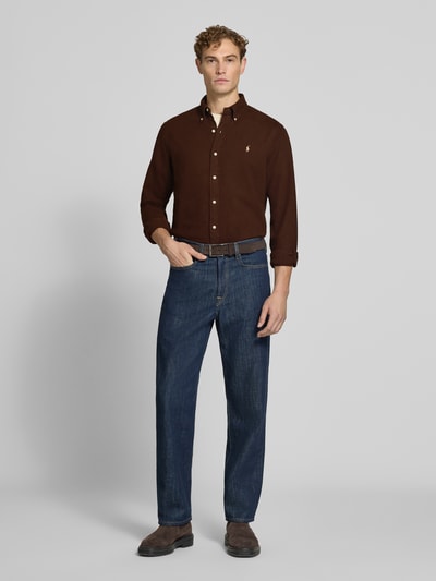 Männermodel trägt das Custom Fit Freizeithemd aus reiner Baumwolle von Polo Ralph Lauren in Dunkelbraun, kombiniert mit Jeans, Ganzkörperansicht von vorne. Kontext: Herren Freizeithemd von Polo Ralph Lauren