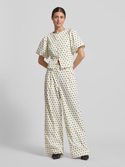 Frauenmodel trägt Slim Fit Bluse mit Puffärmeln Modell 'ANELA DOT' von Neo Noir im Material-Mix mit Stretch-Anteil, Rundhalsausschnitt, weißen Grundton mit schwarzen Punkten, Ganzkörperansicht von vorne.