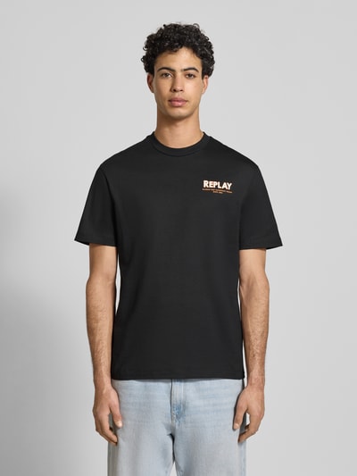 Męski model trägt Regular Fit T-Shirt mit Logo-Stitching von Replay w czerni, napis z przodu, okrągły dekolt, krój regular fit, czysta bawełna, nadruk z napisem, długość tyłu w rozmiarze M: 70 cm, widok całej sylwetki z przodu.