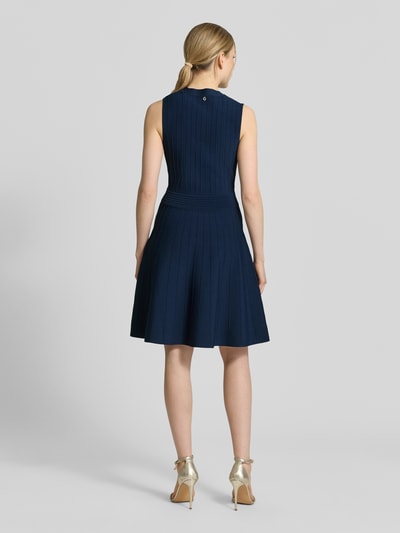 Frauenmodel trägt knielanges Kleid aus Viskose-Mix Modell 'Amber' von Guess in dunklem Blau, taillierte Passform, Strick-Optik, ärmellos, Rückansicht Ganzkörperansicht.