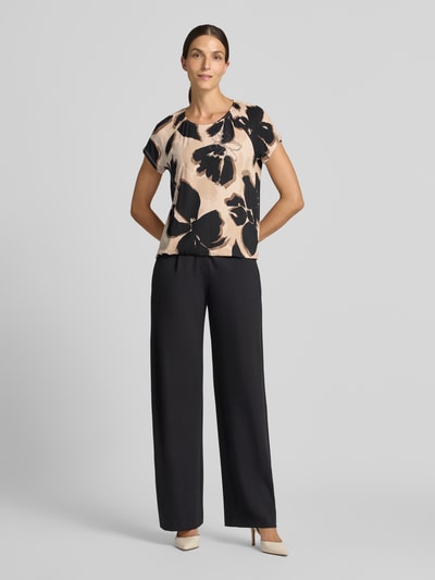 Frauenmodel trägt Regular Fit Kurzarmbluse aus Viskose-Mix Modell 'NOS JULI' von Betty Barclay in Beige mit schwarzen Blumen, Damen Kurzarmbluse, Ganzkörperansicht von vorne.