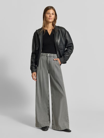 Frauenmodel trägt Slim Fit Longsleeve in Strick-Optik von MYON in Schwarz, kombiniert mit grauer Hose und Lederjacke, Ganzkörperansicht von vorne.