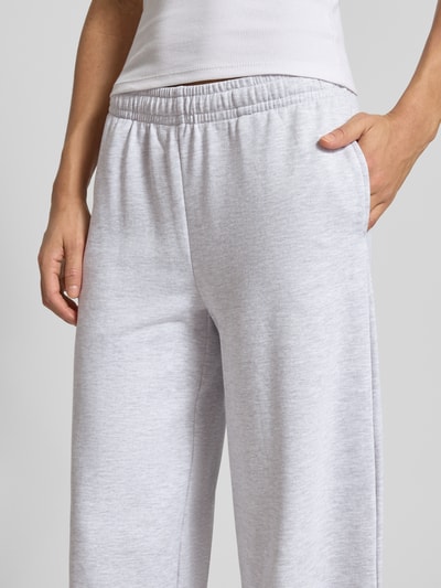 Modelka kobieca nosi Wide Fit Sweatpants mit elastische Bund od Gina Tricot z mieszanki bawełny, krój wide fit, elastyczny pas, krój relaxed fit, długość wewnętrzna nogawki w rozmiarze S 76 cm, jasnoszare, prosta faktura, zbliżenie na biodra i górną część nóg, detal.