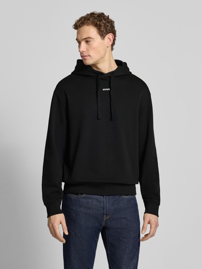 Männermodel trägt Regular Fit Hoodie aus reiner Baumwolle Modell 'DAPO' von HUGO, unifarben schwarz, Sweatstruktur, Ganzkörperansicht von vorne.