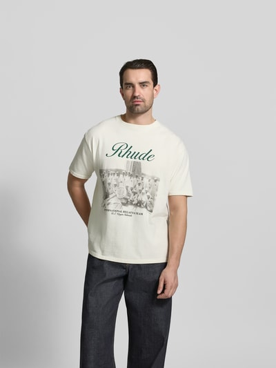 Männermodel trägt Regular Fit T-Shirt aus Baumwolle von RHUDE mit Label-Print und Foto-Print, Rundhalsausschnitt, Ganzkörperansicht von vorne. Rückenlänge bei Größe M: 72 cm.