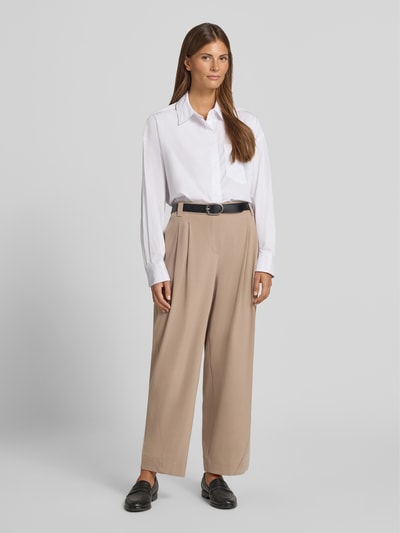 Frauenmodel trägt relaxed Fit Gerade Hose mit Bundfalten Modell 'Metta' von OPUS PANTS in Beige, kombiniert mit weißer Bluse, Ganzkörperansicht von vorne.