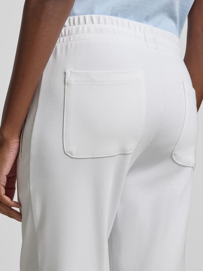Frauenmodel trägt Sweatpants aus Baumwoll-Mix von Juvia in Weiß mit elastischem Bund und Eingrifftaschen; Detailaufnahme Rückansicht. Innenbeinlänge 42 cm, Bundweite 67 cm, schmal zulaufendes Bein, elastische Abschlüsse.
