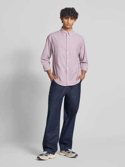 Męski model nosi Regular Fit Freizeithemd mit Brusttasche Modell 'NORREBRO' von Jack & Jones, bawełniany miks, krój regular fit, z kieszenią na piersi, kołnierzem button-down, listwą guzikową, długość pleców w rozmiarze M: 74 cm, szerokość ramion w rozmiarze M: 52 cm, długość rękawa w rozmiarze M: 60 cm, czerwona koszula, granatowe spodnie, kremowe buty, widok całej sylwetki z przodu