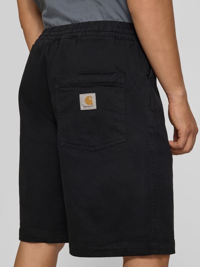 Mannenmodel draagt Shorts uit katoenmix Model 'Floyde' van Carhartt Work In Progress, relaxed fit, elastische band met tunnelkoord, steekzakken, bandwijdte maat M 39 cm, binnenbeenlengte maat M 25 cm, zwarte kleur, rechte lijnen en gladde textuur. Ganzkörperansicht Rückansicht.