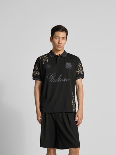 Männermodel trägt Poloshirt floralem Allover-Stitching von Don’t Waste Culture in Schwarz mit Logo-Print, Polokragen, Relaxed-Fit, Kurzärmelig, Ganzkörperansicht von vorne.