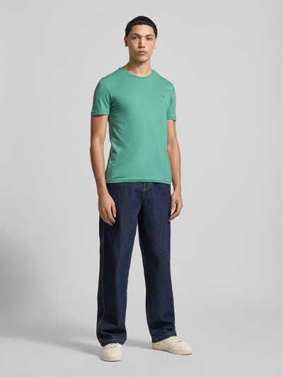 Männermodel trägt Slim Fit T-Shirt aus Baumwoll-Mix Modell 'JASPE HERITAGE' von Tommy Jeans in Melange-Optik, Logo-Stitching, Ganzkörperansicht von vorne.