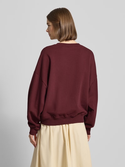 Frauenmodel trägt Sweatshirt mit Statement-Print und überschnittenen Schultern von OH APRIL in dunklem Rot, Reine Baumwolle, Regular-Fit, Gerippter Rundhalsausschnitt, Gerippte-Abschlüsse, Ganzkörperansicht Rückansicht.