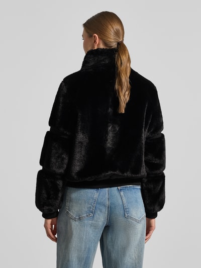 Frauenmodel trägt Jacke mit Teddyfell und gerippten Abschlüssen von Guess, Schwarz, gerader Schnitt, Stehkragen, Ganzkörperansicht Rückansicht. Rückenlänge 56 cm, Schulterbreite 38 cm, Brustweite 53 cm, Ärmellänge 61 cm.