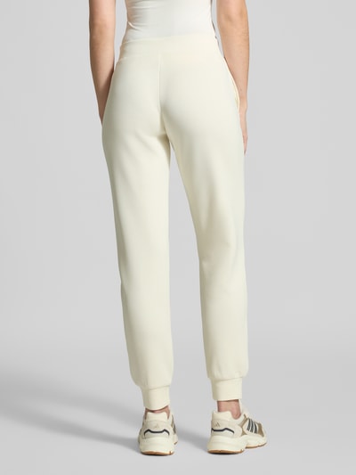 Modelka nosi Sweatpants mit Label-Detail von Guess Activewear, kremowy kolor, elastyczny materiał z domieszką modalu, prosty krój, elastyczny pas, kieszenie boczne, detal z logo, widok całej sylwetki z tyłu.