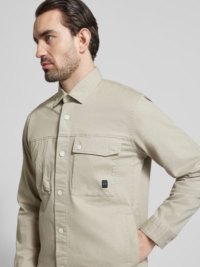 Męski model nosi Regular Fit Hemdjacke mit Brusttaschen od camel active, bawełniany miks ze stretchem, krój regular fit, kolor beżowy, guzik, kieszenie na piersi, kent kołnierzyk, Szerokość w rozmiarze M: 58 cm, długość tyłu: 74 cm, szerokość ramion: 47 cm, długość rękawa: 66 cm, zdjęcie z przodu, zbliżenie na górę sylwetki.