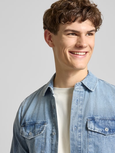 Męski model nosi Slim Fit Freizeithemd aus reiner Baumwolle Modell 'Marine' von G-Star Raw, jasnoniebieski dżins, przód z kieszeniami na piersi, krój slim fit, bawełna, kent kołnierzyk, długość tyłu w rozmiarze M: 75 cm, szerokość w rozmiarze M: 40 cm, długość rękawa w rozmiarze M: 67 cm, detal z logo, zbliżenie górnej części tułowia.
