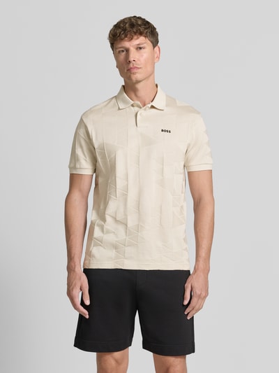 Męski model nosi koszulkę polo Regular Fit Poloshirt model 'PL_NETWORK JQ PIRAX' od BOSS Green w kolorze beżowym, geometryczna faktura, czarna aplikacja z logo, krój regular fit, widok całej sylwetki z przodu.