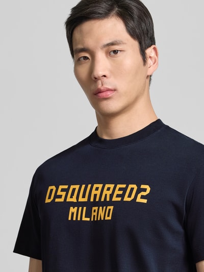 Männermodel trägt Cool Fit T-Shirt aus reiner Baumwolle von Dsquared2, dunkle Farbe, gelber Statement-Print, Nahaufnahme Oberkörper.