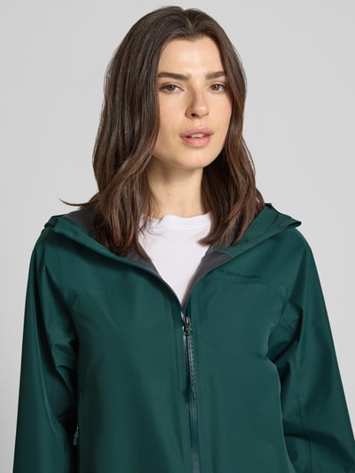 Frauenmodel trägt Regular Fit Jacke mit Logo-Print Modell 'Treeline' von PEAK PERFORMANCE in Dunkelgrün, glatte Textur, Nahaufnahme Oberkörper, Rückenlänge bei Größe S: 71 cm, Schulterbreite: 44 cm, Brustweite: 53 cm, Ärmellänge: 55 cm, Stehkragen mit Kapuze.