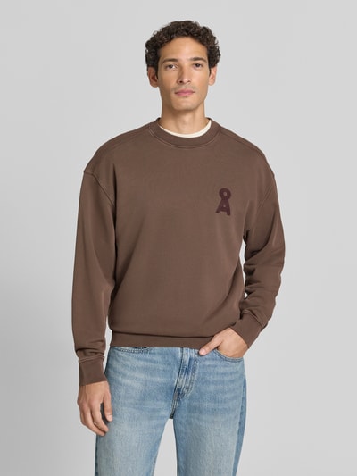 Männermodel trägt braunes Relaxed Fit Sweatshirt aus reiner Baumwolle Modell 'ICONIC Å' von ARMEDANGELS, kombiniert mit blauen Jeans, Nahaufnahme Oberkörper, Herren Sweatshirt von ARMEDANGELS.