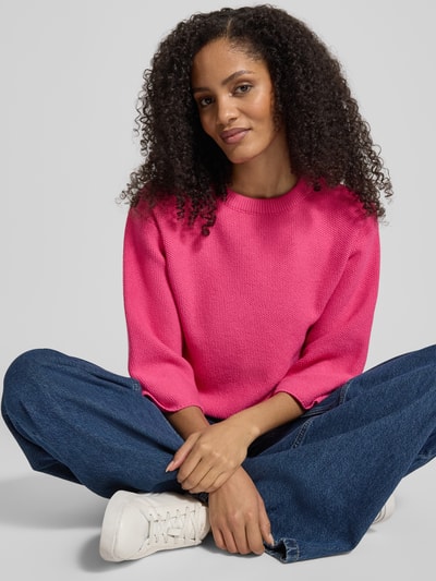 Kobiece modelka nosi Oversized Strickpullover aus Viskose-Mix mit Stehkragen von More & More, mieszanka wiskozy, krój oversized, stójka, opuszczone ramiona, długość tyłu 51 cm, długość rękawów 41 cm, intensywny róż, prosta faktura, jasnoniebieskie spodnie, białe buty, zdjęcie całej sylwetki z przodu.