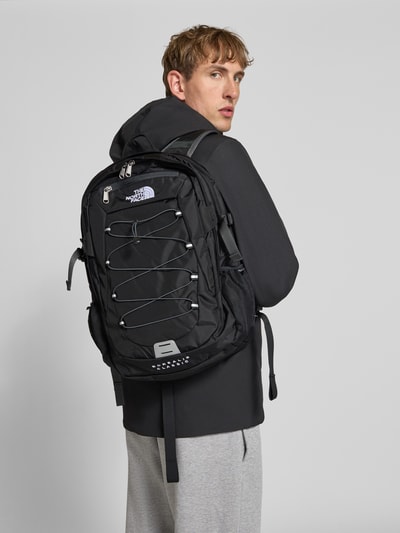 Männermodel trägt Rucksack mit Logo-Stitching Modell 'BOREALIS' von The North Face, schwarz, geteiltes Hauptfach, Rückansicht, KI-modifiziertes Bild.
