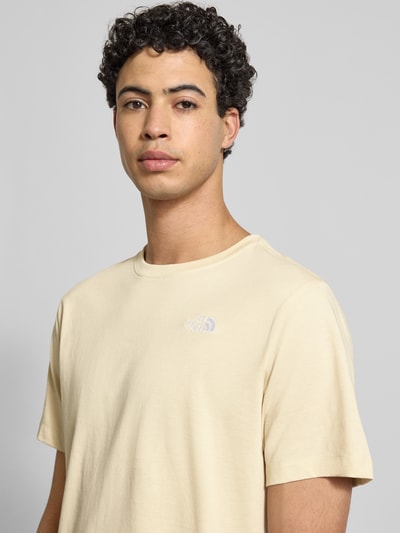 Männermodel trägt Regular Fit T-Shirt aus Baumwoll-Mix Modell 'EVOLUTION' von The North Face in Beige mit Label-Detail, Nahaufnahme Oberkörper. Rückenlänge bei Größe M: 71 cm.