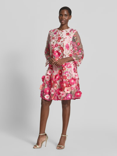 Frauenmodel trägt Knielanges Cocktailkleid mit Stitchings Modell 'FLOWERING' von YAS, A-Linie, Semitransparent, 3/4-Arm, Rundhalsausschnitt, florale Muster in Rosa- und Pinktönen, Strukturmix, Ganzkörperansicht von vorne. Rückenlänge bei Größe 36: 93 cm, Brustweite bei Größe 36: 47 cm, Ärmellänge bei Größe 36: 51 cm.