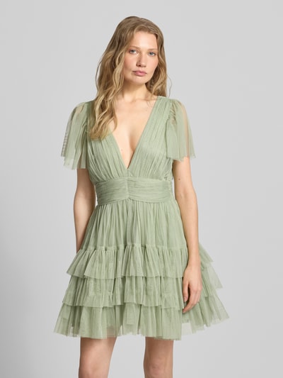 Frauenmodel trägt Cocktailkleid mit tiefem V-Ausschnitt von LACE & BEADS aus grünem Tüll, A-Linie, Stufen-Look, Minikleid, Nahaufnahme Oberkörper.