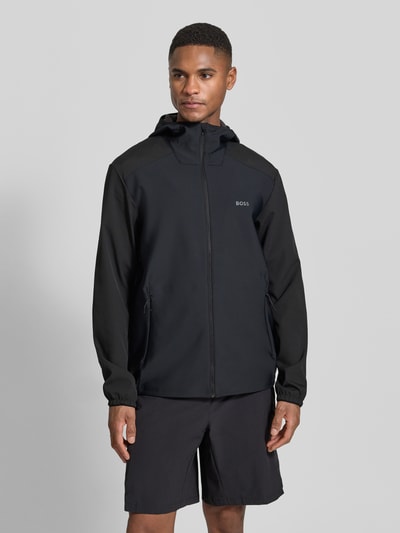 Männermodel trägt Regular Fit Softshell-Jacke mit Kapuze Modell 'LW_Cruiselite' von BOSS Green in Schwarz, Reißverschluss, Langarm, Ganzkörperansicht von vorne.