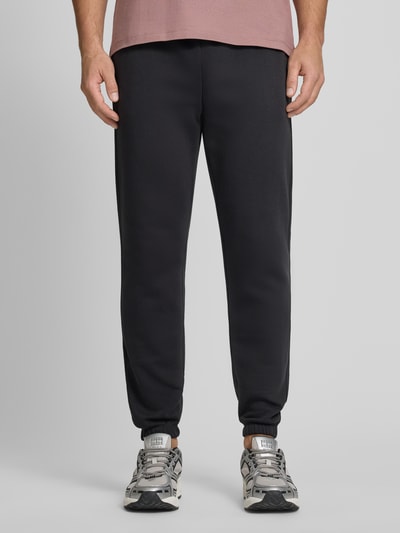 Männermodel trägt Sweatpants mit Logo und elastischem Bund von GAP aus Baumwoll-Mix, Regular-Fit, schwarze Farbe, Ganzkörperansicht von vorne.