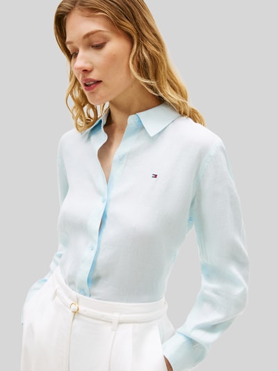 Frauenmodel trägt Relaxed Fit Langarmbluse aus reinem Leinen von Tommy Hilfiger, Optik: Unifarben, Passform: Relaxed-Fit, Hemdkragen, Logo-Stitching, einreihige Knopfleiste, Ärmelform: Langarm, Ärmelabschluss: Manschette, Rumpfabschluss: abgerundet, Materialverarbeitung: Flammgarn, Material: Leinen, hellblau, glatte Textur, Nahaufnahme Oberkörper.