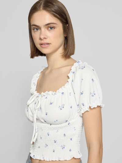 Frauenmodel trägt Slim Fit Blusentop mit Allover-Muster Modell 'HILLARY' von Only, weiß-blau, Struktur mit floralem Muster, Henley-Ausschnitt, Kurzarm, Cropped-Länge, Raffungen am Ärmelabschluss, Ganzkörperansicht von vorne.