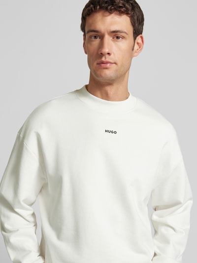 Männermodel trägt Regular Fit Sweatshirt aus reiner Baumwolle Modell 'DAPOCREW' von HUGO in Weiß mit Rundhals und Label-Schriftzug, Nahaufnahme Oberkörper.