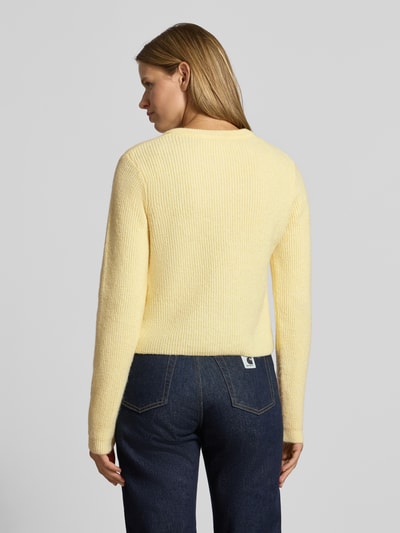 Frauenmodel trägt Strickjacke mit Woll-Anteil Modell 'SILLY' von PIECES, hellgelb, grobe Stricktextur, kombiniert mit Jeans, Ganzkörperansicht Rückansicht.