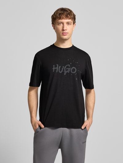 Männermodel trägt Regular Fit T-Shirt aus reiner Baumwolle Modell 'NIEROFIX_U261' von HUGO, Optik: Unifarben, Motiv-Print, Rundhals, Kurzarm, Label-Stitching-Applikation, Ganzkörperansicht von vorne.