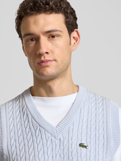 Männermodel trägt Regular Fit Pullunder aus Baumwoll-Mix von Lacoste in Hellblau, Zopfmuster, Logo-Detail, Nahaufnahme Oberkörper