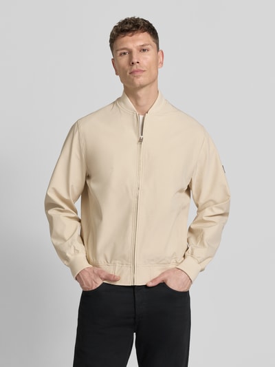 Männermodel trägt Bomberjacke mit Stehkragen Modell 'BLAASPEN' von Jack & Jones Premium, Material-Mix mit Stretch-Anteil, lockerer Schnitt, Reißverschluss, seitliche Eingrifftaschen, elastische Abschlüsse, hellbeiger Farbton, glatte Textur, Ganzkörperansicht von vorne.