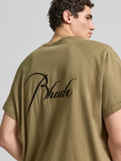 Männermodel trägt Regular Fit T-Shirt aus reiner Baumwolle von RHUDE in Khaki mit Label-Stitching, Raglanärmel, Rückenlänge 69 cm, Ganzkörperansicht Rückansicht.