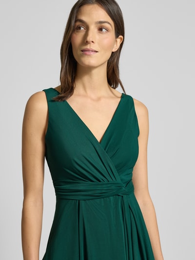 Modelka kobieca nosi zielone, taliowane cocktailkleid mit V-Ausschnitt od TROYDEN COLLECTION, widoczne drapowania, pasek, podszewka, zbliżenie na górną część ciała.