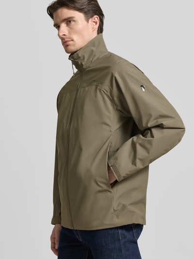 Männermodel trägt Softshell-Jacke mit Label-Details von PEAK PERFORMANCE in Oliv, gerader Schnitt, Stehkragen, Reißverschluss, Ganzkörperansicht von vorne.