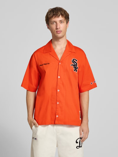 Männermodel trägt Relaxed Fit Freizeithemd aus Baumwoll-Mix von Champion in Orange mit Statement-Stitching, Kurzarm, Reverskragen, Ganzkörperansicht von vorne.