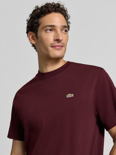 Männermodel trägt Regular Fit T-Shirt aus reiner Baumwolle von Lacoste in Dunkelrot, glatte Textur, Nahaufnahme Oberkörper. Herren T-Shirt von Lacoste.
