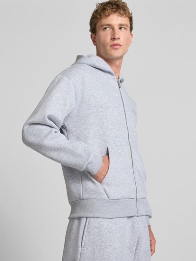 Männermodel trägt Regular Fit Sweatjacke aus Baumwoll-Mix von REVIEW in Hellgrau mit Känguru-Tasche und Reißverschluss, Ganzkörperansicht von vorne.