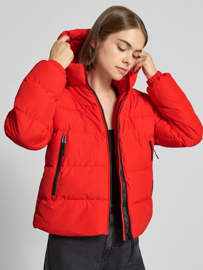Vrouwenmodel draagt Regular Fit Jacke in Stepp-Optik van Superdry in felrood met zwarte ritssluiting en tunnelkoord capuchon, Ganzkörperansicht van voren. Ruglengte bij maat S: 58 cm, schouderbreedte 46 cm, borstwijdte 52 cm, mouwlengte 64 cm.