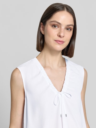 Frauenmodel trägt Regular Fit Bluse mit Zierschleife von Marc Cain in Weiß, V-Ausschnitt, Tunnelzug, Ärmelloses-Design, Nahaufnahme Oberkörper.
