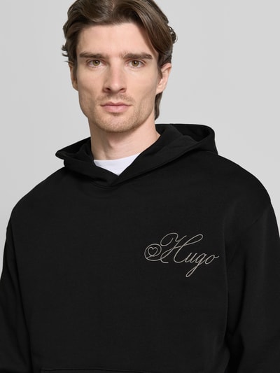 Männermodel trägt Regular Fit Hoodie aus reiner Baumwolle Modell 'DALENTO' von HUGO in Schwarz mit Label Stitching, Nahaufnahme Oberkörper.