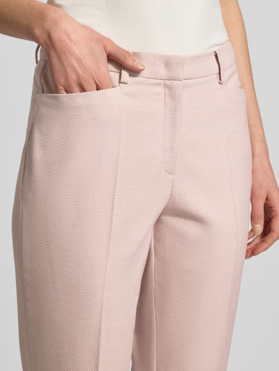 Kobiece modelka nosi Spodnie z kantami i wpuszczanymi kieszeniami od More & More, mieszanka materiałów z dodatkiem wiskozy, krój slim fit, wpuszczana kieszeń, kieszeń z tyłu, kolor jasnoróżowy, szczegóły szwów, szerokość w rozmiarze 36: 39 cm, długość wewnętrzna nogawki w rozmiarze 36: 75 cm, zbliżenie na górną część ciała.